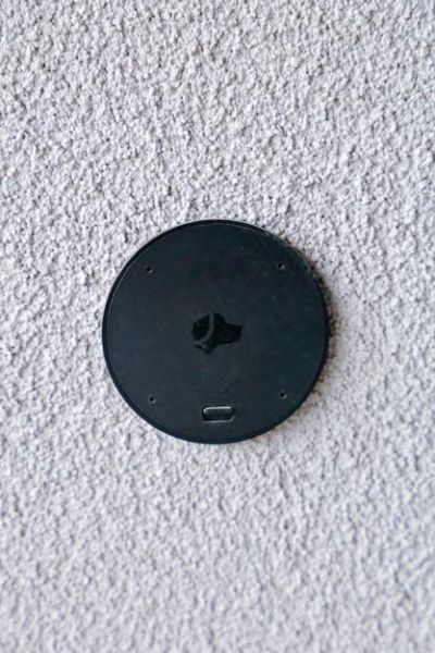 A round, black sensor device mounted on a light-colored wall, blending seamlessly with the surface.