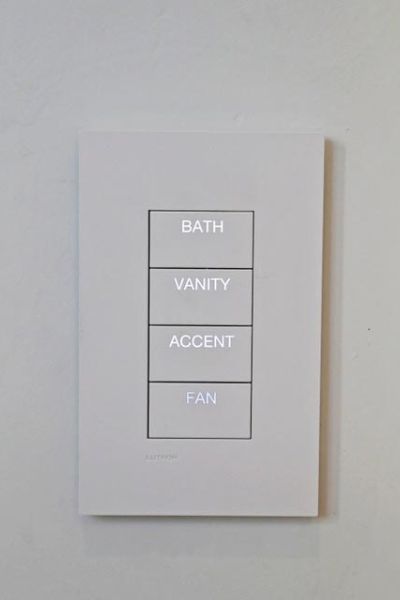 A minimalist control panel with four buttons labeled for lighting and fan settings in a bathroom.
