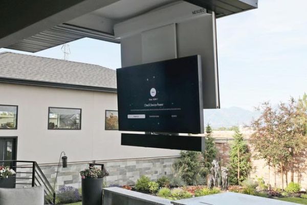 An outdoor entertainment area featuring a large flat-screen TV mounted under a covered patio, overlooking a landscaped yard.
