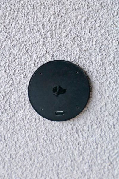 A round, black sensor device mounted on a light-colored wall, blending seamlessly with the surface.