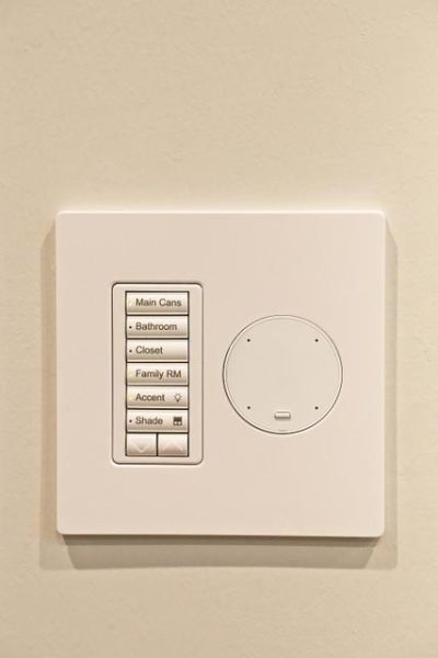 Wall-mounted control panel with multiple labeled buttons for different room lights and shades.