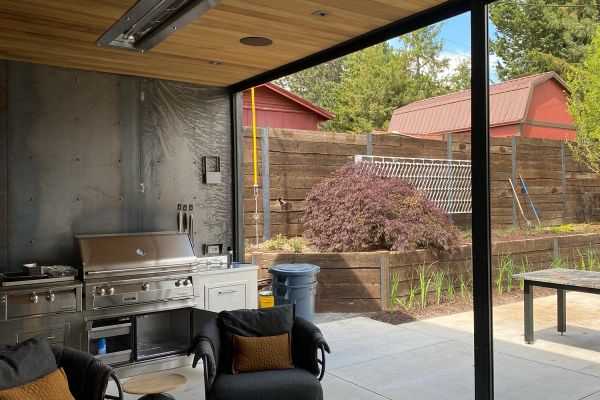 Outdoor living area featuring a modern kitchen setup with a grill, seating, and open access to a backyard.