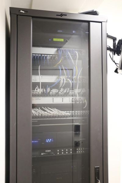 A network rack with various connected devices and cables, enclosed in a black cabinet with a glass door.