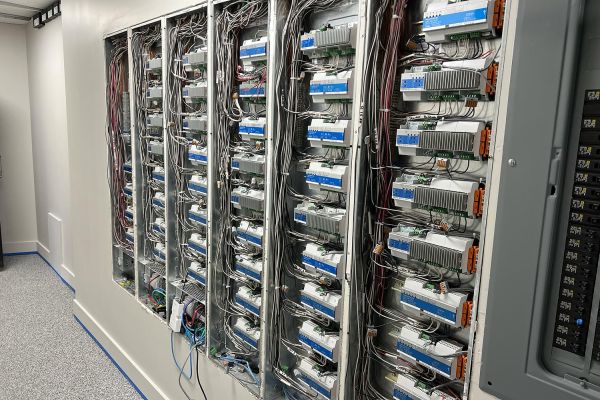 Room with several open electrical panels filled with wiring and electronic components.