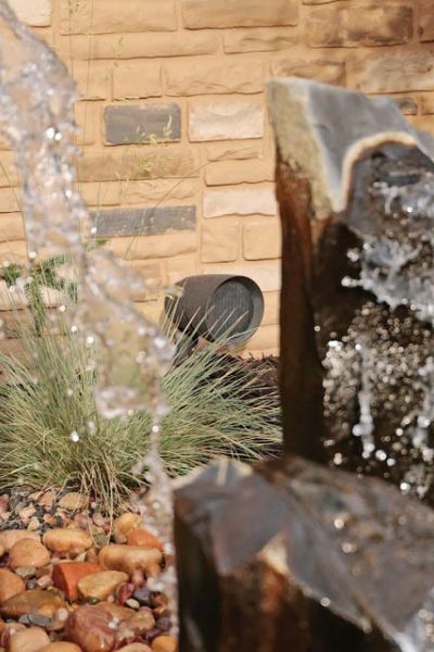 Water feature with a vertical stone fountain and a small outdoor speaker visible in a landscaped garden.