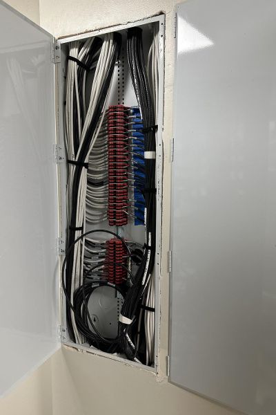 An open electrical panel mounted on a wooden exterior wall, showing circuit breakers and wiring.