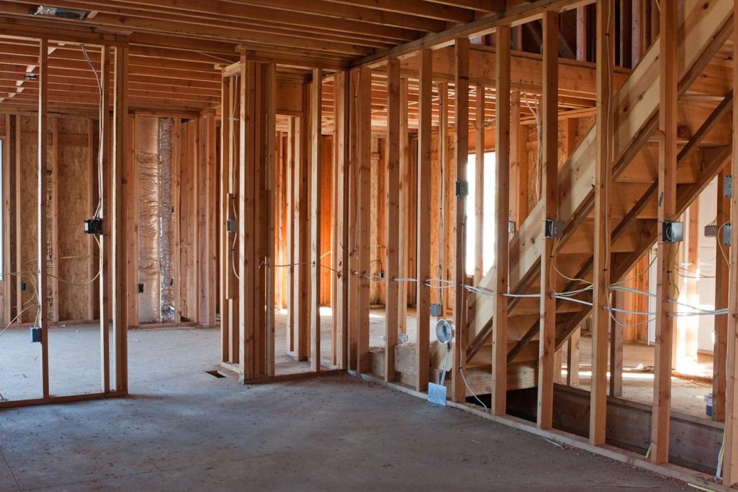 A house under construction, showing exposed wooden framing, wiring, and partially installed infrastructure.