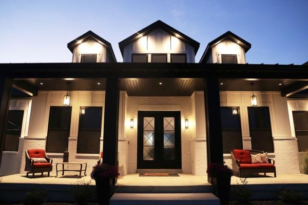 A front view of a house at twilight, showcasing a well-lit porch and outdoor seating.