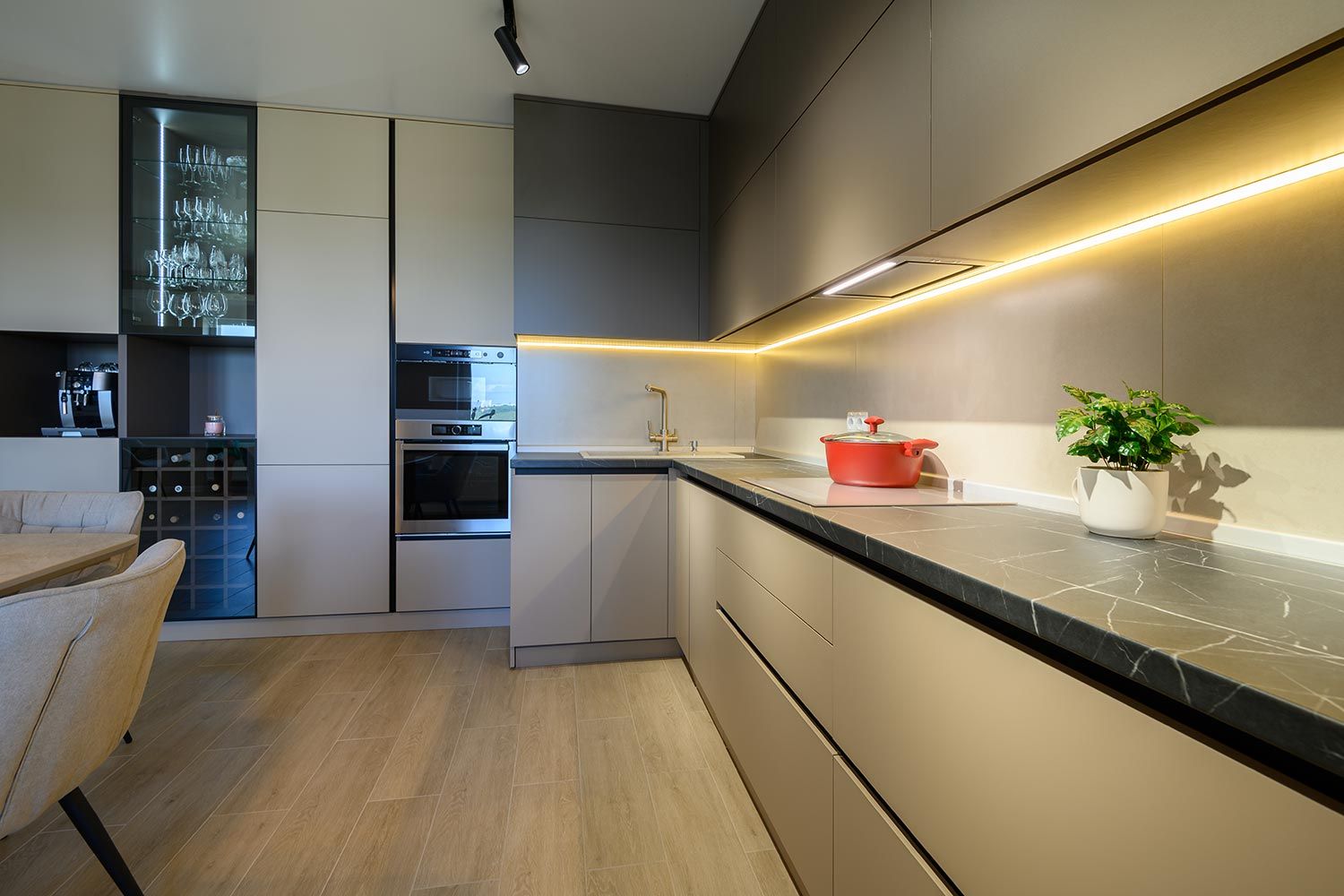 A modern kitchen with sleek cabinets, a black countertop, under-cabinet LED lighting, and a red pot on the stove.