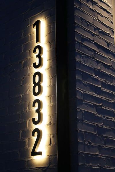 Illuminated house numbers mounted on a brick wall, creating a clear and stylish display.