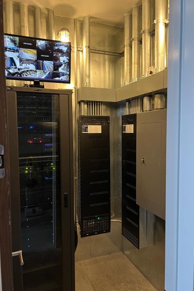 A utility room with metal walls and a security monitoring system displaying multiple camera feeds on a wall-mounted screen.