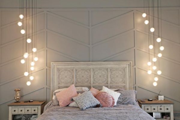 A bedroom with a patterned wall, featuring pendant lights hanging on both sides of a bed with decorative pillows.