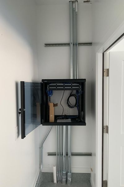 Wall-mounted network cabinet with organized cabling and conduits.