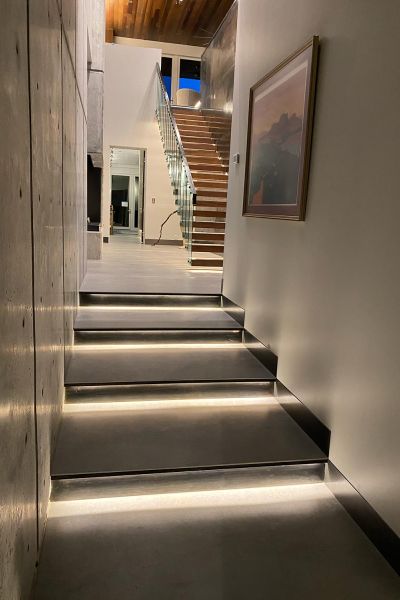 A modern hallway with illuminated steps leading to an upper floor, featuring a concrete wall and a framed picture.