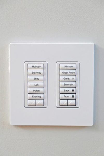 A wall-mounted control panel with labeled buttons for lighting settings in different areas of a home.