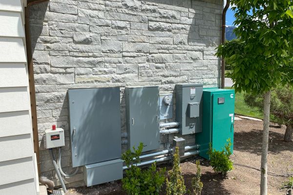 Outdoor electrical setup with multiple control boxes and a green generator against a stone wall.