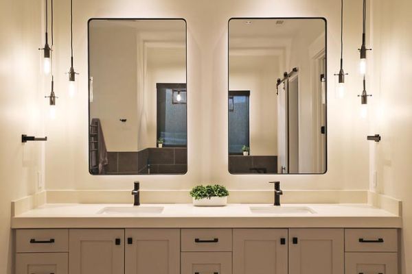 A modern bathroom with a double vanity, illuminated by hanging pendant lights and two large mirrors.