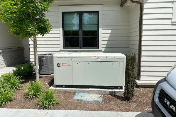 Large outdoor generator installed next to an HVAC unit and a white building.