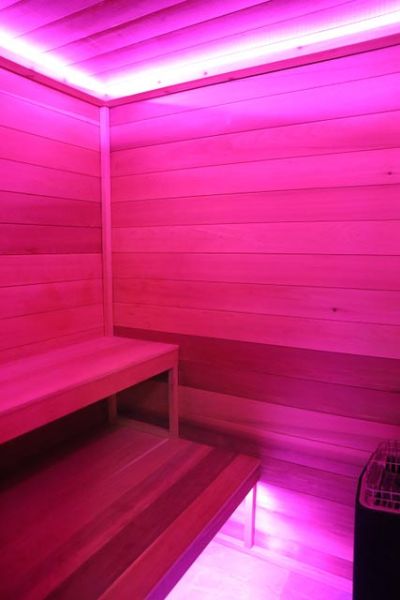 A wooden sauna interior with vibrant pink lighting creating a relaxing atmosphere.