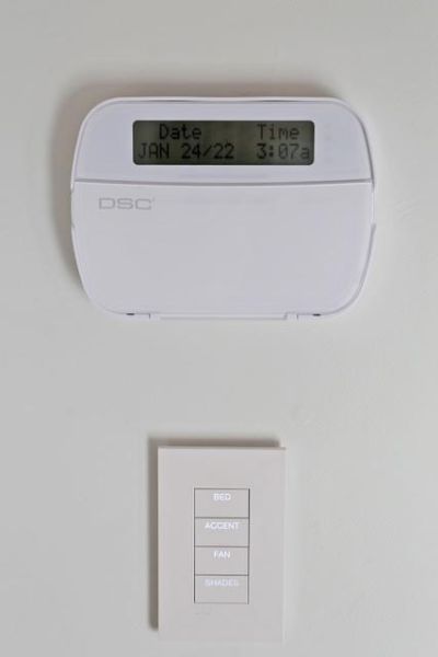 Wall-mounted light switch with buttons labeled for Bed, Accent, Fan, and Shades, positioned below a digital thermostat.