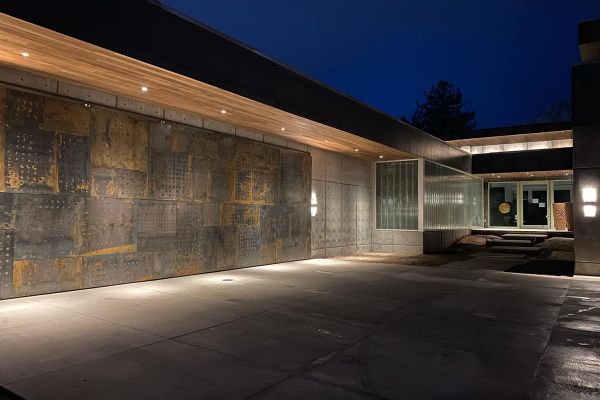 Modern home with a unique metal wall design and under-roof lighting at night.