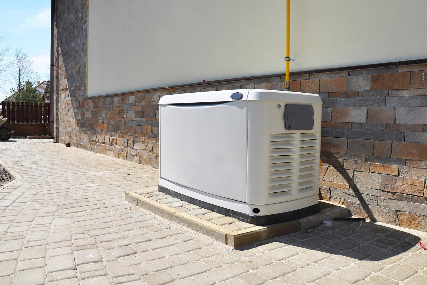 A large white generator installed outside a building with stone siding and a paved pathway.