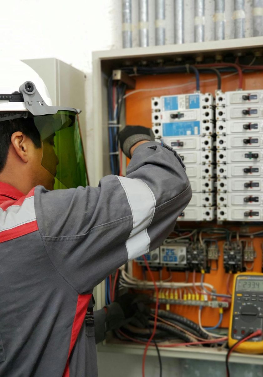 Electrician wearing safety gear working on a residential electrical panel with multiple circuit breakers.