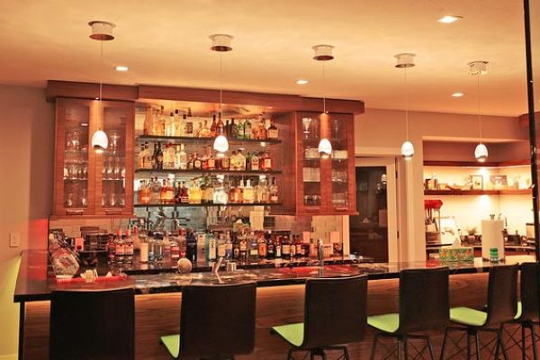 A cozy bar area with warm lighting, featuring pendant lights above a well-stocked counter with various bottles and glasses.