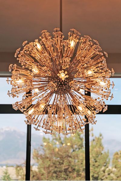 A dazzling chandelier with intricate crystal details, shaped like a burst of light, hangs against a window backdrop with a scenic view.