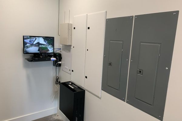 Interior room with a wall-mounted monitor displaying security footage and multiple electrical panels.