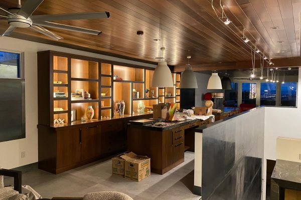 A spacious room with wooden cabinetry and pendant lights, featuring a built-in desk and shelving with decorative items.